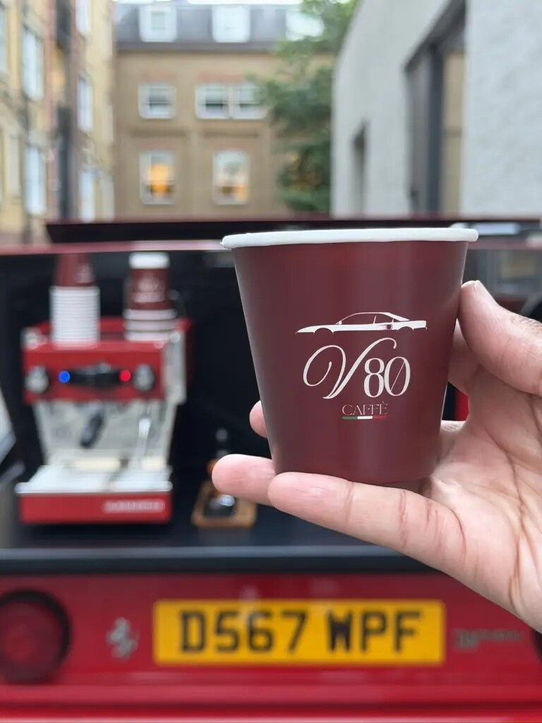 A V80 branded espresso held in front of the Ferrari coffee bar